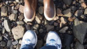 Xtratuf boots and tennis shoes face each other on beach rocks