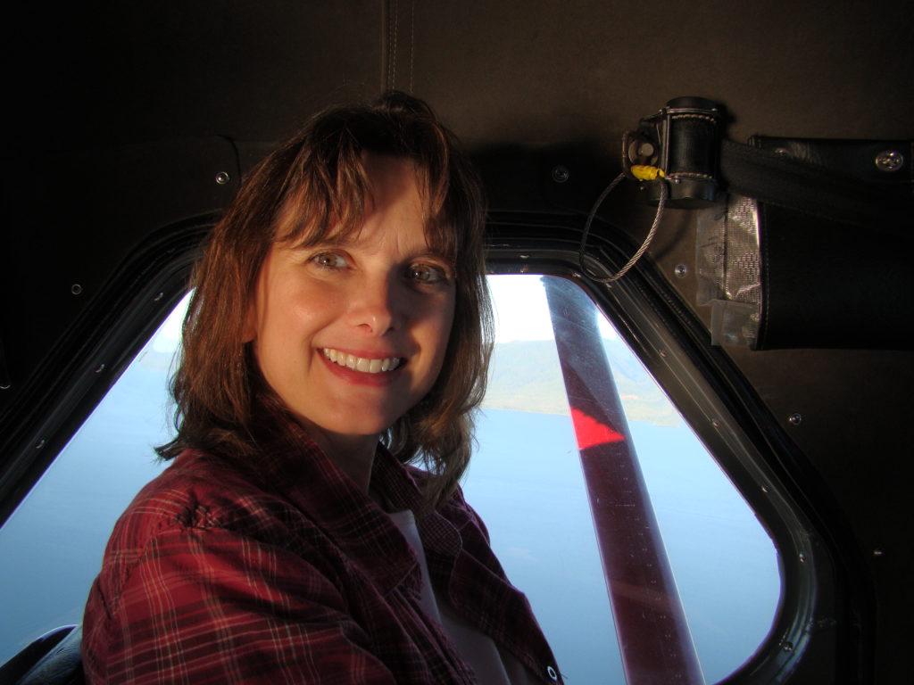 Melissa Cook rides on a floatplane with the water visible outside the window behind her.