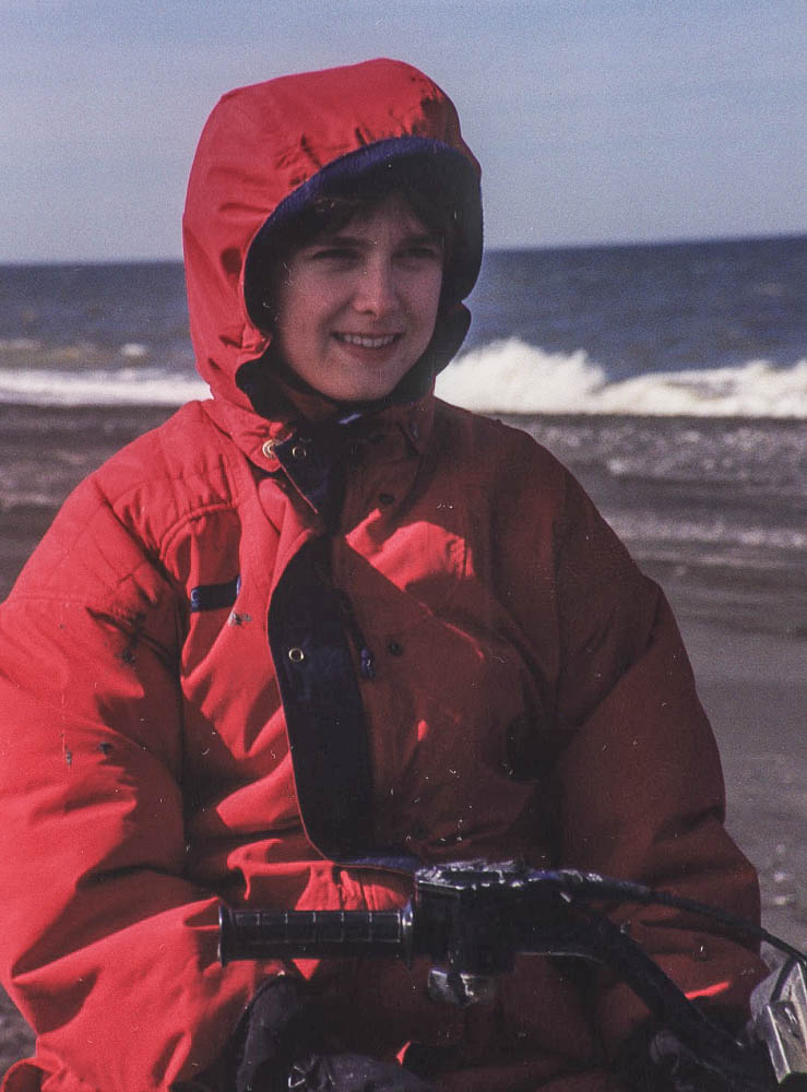 Melissa Cook sitting on a four-wheeler in a red coat bundled up on the Bering Sea