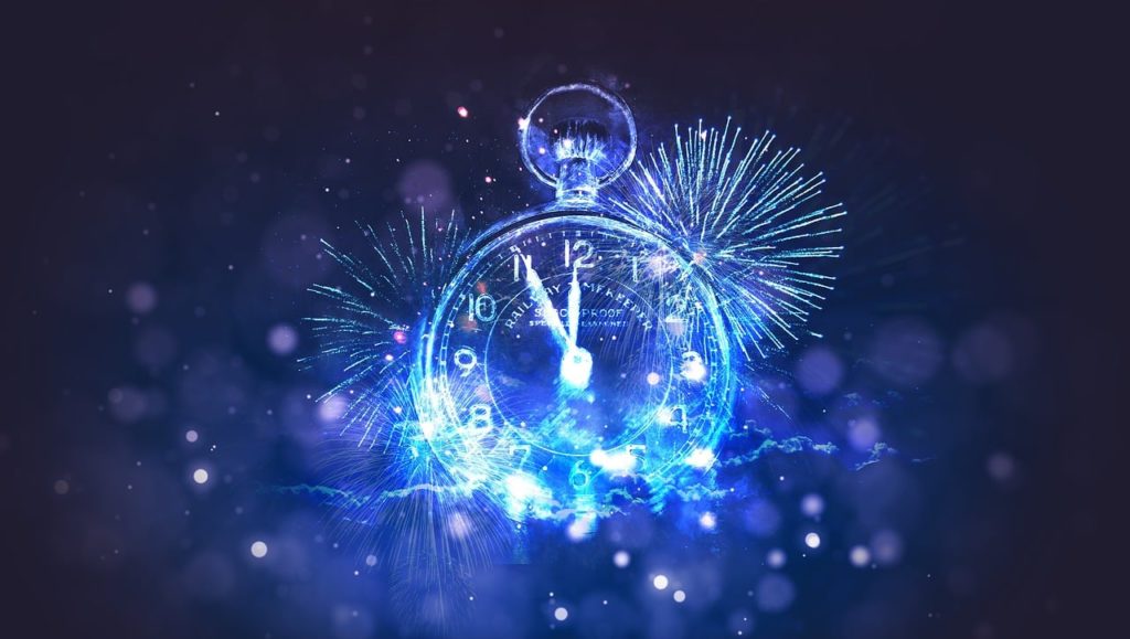 A clock in Christmas lights with fireworks in the background for New Years