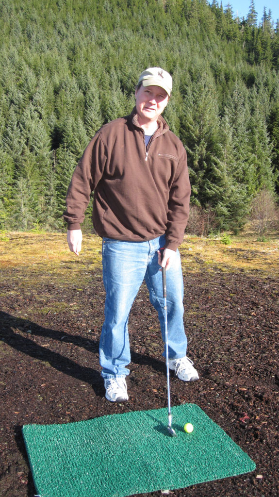 Elgin Cook stands at his golf mat with a club at the old Thorne Bay, Alaska dump
